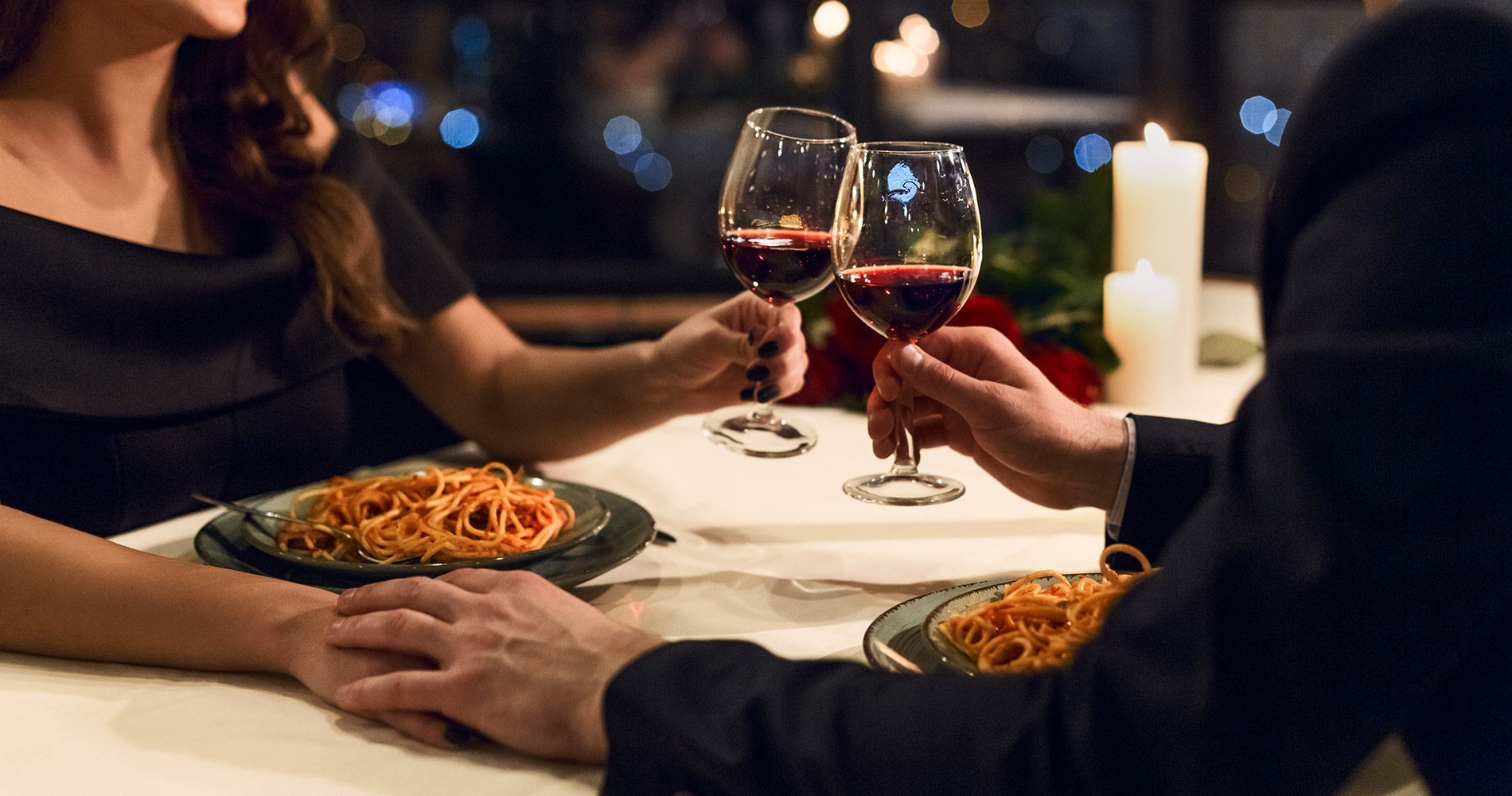 Coppia elegante al tavolo, con piatti di spaghetti e calici di vino rosso